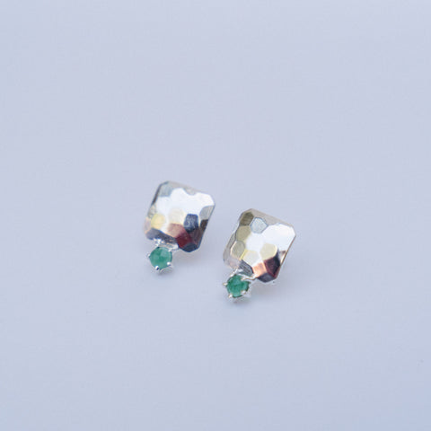 A pair of silver-toned geometric stud earrings with a hammered finish and small green gemstone accents, displayed on a light gray background.