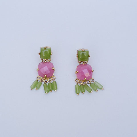 A pair of gold-plated drop earrings featuring a faceted pink stone, a rectangular green stone, and dangling green beads, set against a plain light gray background.
