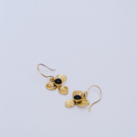 A pair of gold dangle earrings shaped like stylized flowers with textured petals and a small black center, shown on a plain light gray background.